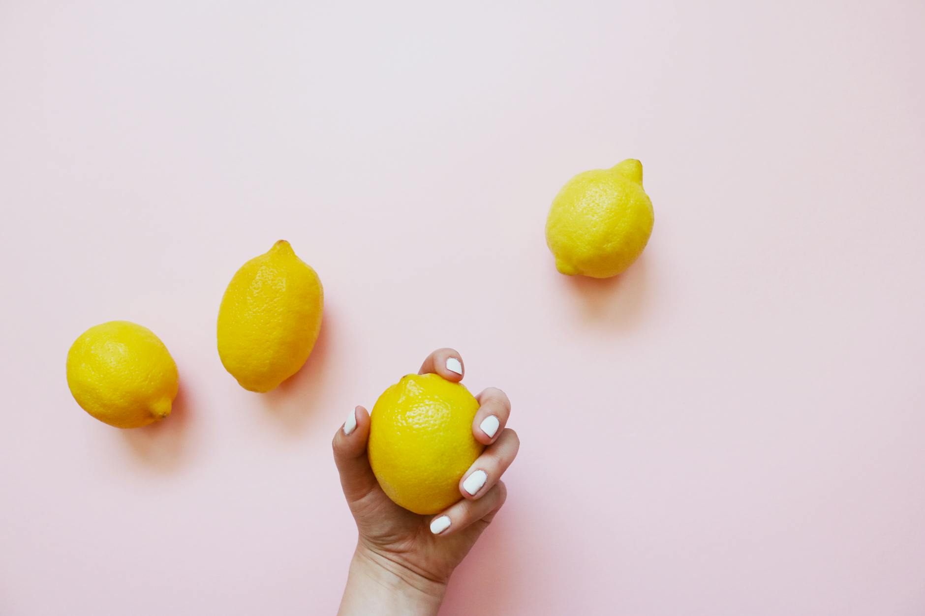 A hand holding a fresh lemon on a soft pink background with additional lemons, symbolizing gentle, natural stimulation