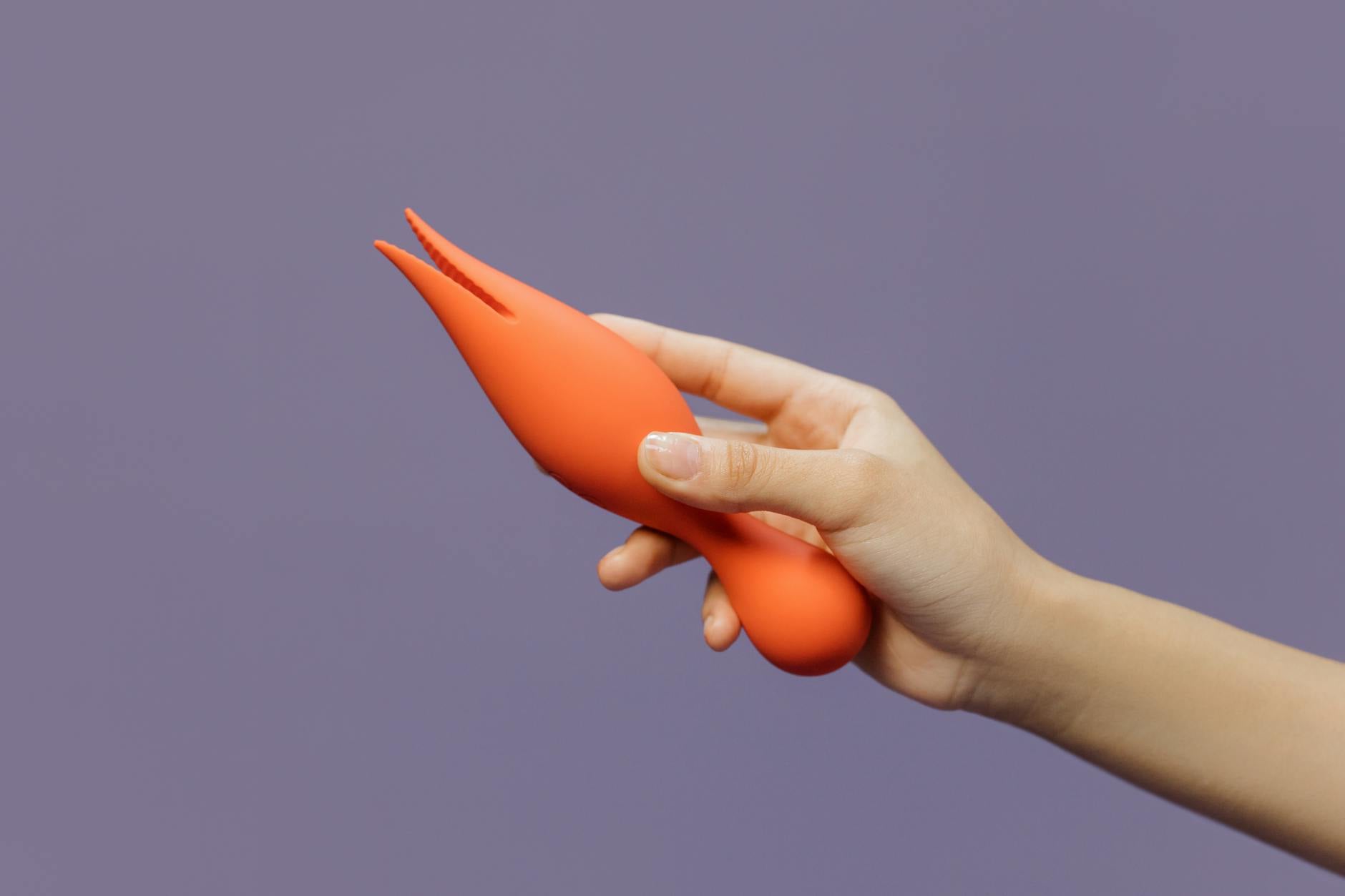 Close-up of a hand holding a lemon clitoral vibrator against a minimalistic purple backdrop, showcasing modern sensuality
