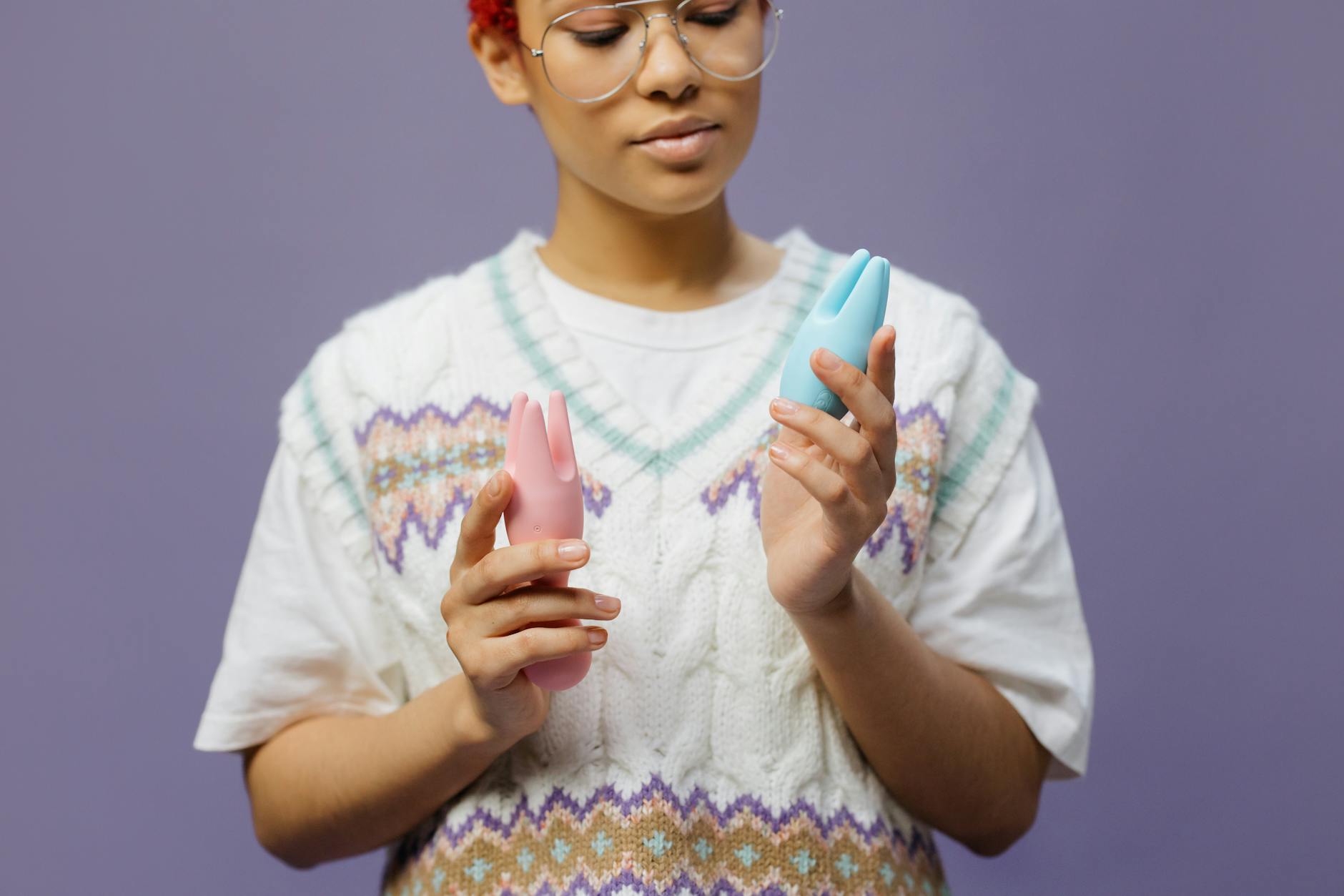 Woman holding blue and pink silicone vibrators in a contemplative pose
