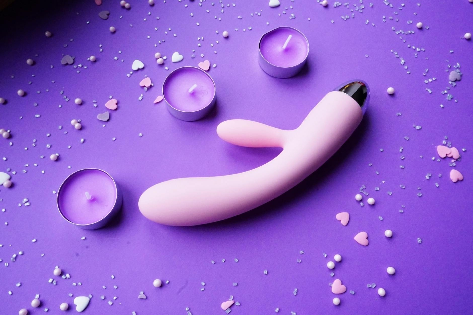 Pink lemon clitoral vibrator on a purple background with romantic candles and heart confetti
